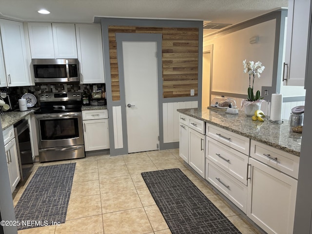 kitchen with light stone counters, decorative backsplash, white cabinets, visible vents, and stainless steel appliances