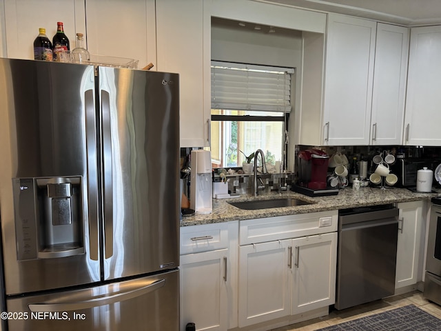 kitchen with light stone countertops, a sink, stainless steel appliances, decorative backsplash, and white cabinets