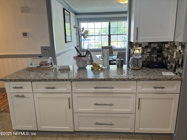 kitchen featuring white cabinets, a peninsula, light stone countertops, and decorative backsplash