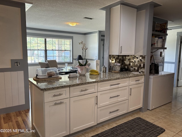 kitchen with light stone counters, white cabinetry, light tile patterned flooring, a peninsula, and backsplash