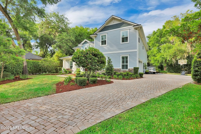 view of front of home featuring a front lawn, stone siding, decorative driveway, and an attached garage