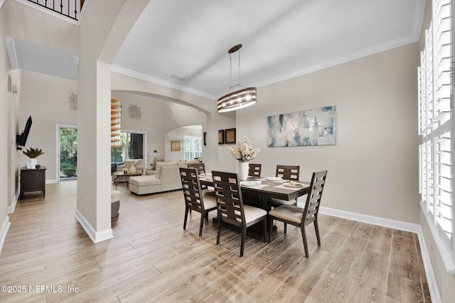 dining area featuring light wood-style flooring, baseboards, ornamental molding, and arched walkways