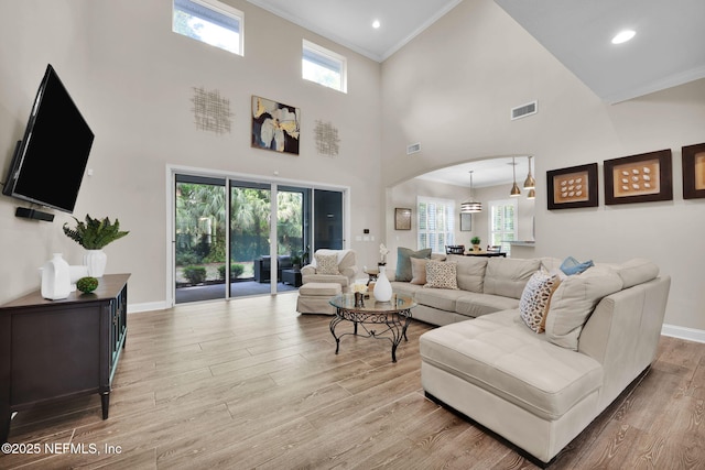 living area with arched walkways, light wood-type flooring, baseboards, visible vents, and crown molding