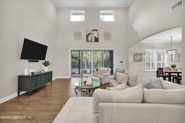 living area featuring visible vents, baseboards, arched walkways, wood finished floors, and a high ceiling