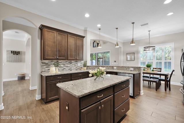 kitchen with decorative backsplash, visible vents, a center island, light wood finished floors, and a peninsula