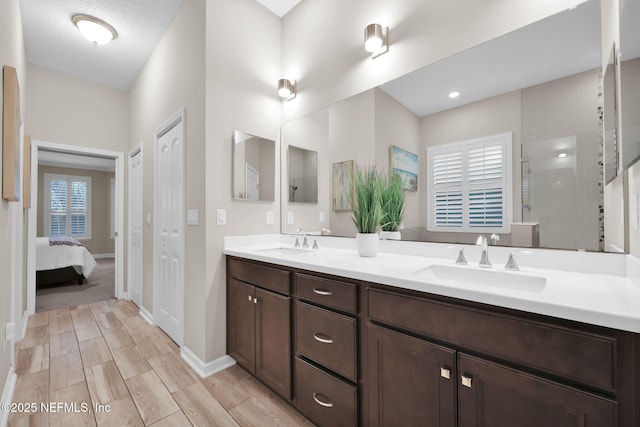 ensuite bathroom featuring baseboards, walk in shower, double vanity, and a sink