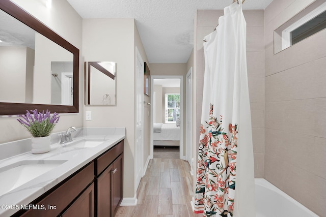 bathroom with wood finished floors, ensuite bath, double vanity, a sink, and baseboards