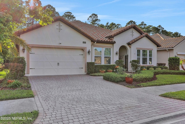 mediterranean / spanish house with an attached garage, decorative driveway, stucco siding, and a tiled roof