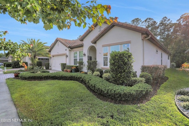 mediterranean / spanish-style home with a tile roof, a front lawn, an attached garage, and stucco siding