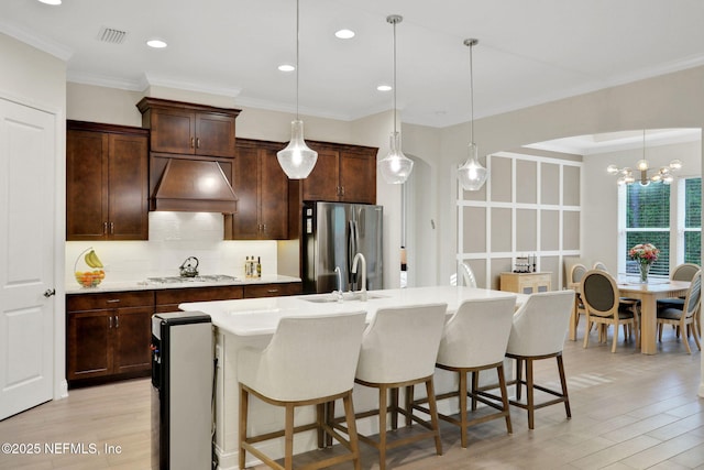 kitchen with custom range hood, freestanding refrigerator, light wood finished floors, gas stovetop, and backsplash