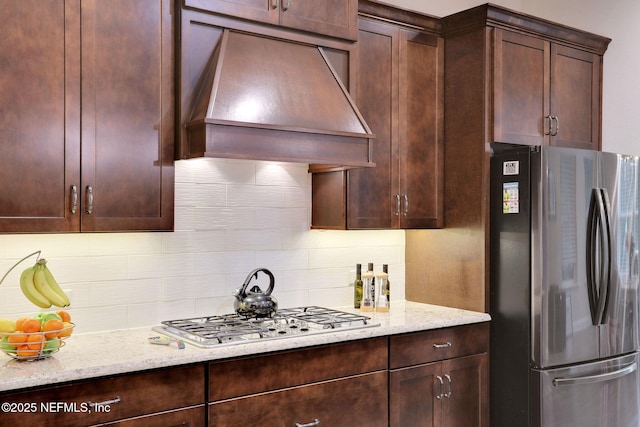 kitchen with dark brown cabinetry, tasteful backsplash, light stone countertops, custom range hood, and appliances with stainless steel finishes