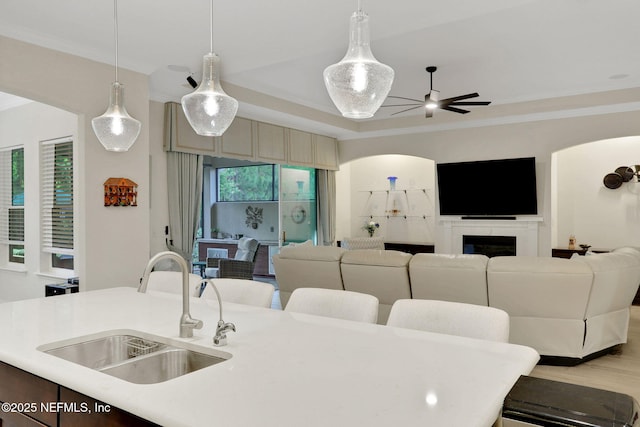 interior space featuring a sink, light countertops, open floor plan, an island with sink, and a ceiling fan