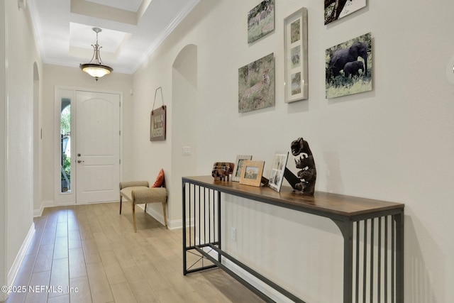 foyer featuring arched walkways, light wood finished floors, baseboards, a raised ceiling, and crown molding