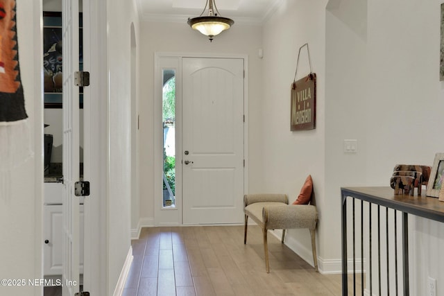 foyer entrance featuring crown molding, arched walkways, baseboards, and light wood-style floors