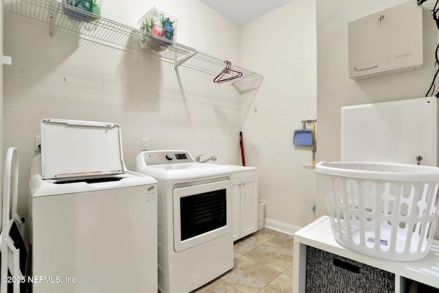 laundry area featuring light tile patterned flooring, separate washer and dryer, cabinet space, and baseboards