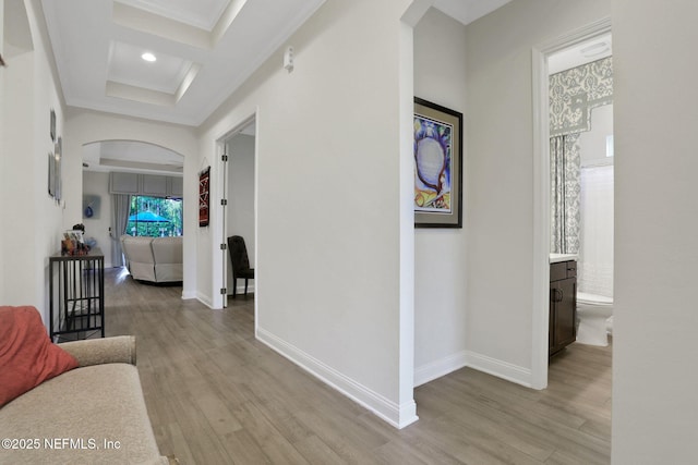 hallway featuring light wood-style floors, baseboards, ornamental molding, and arched walkways