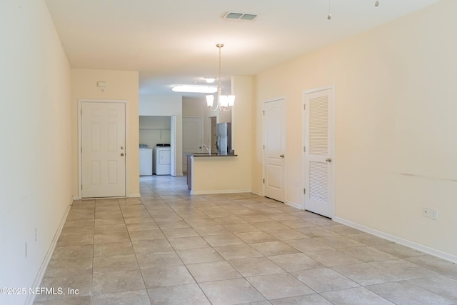 empty room with washer and dryer, baseboards, an inviting chandelier, and light tile patterned floors