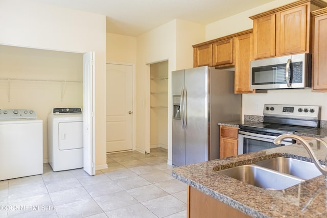 kitchen with brown cabinetry, separate washer and dryer, a sink, appliances with stainless steel finishes, and light tile patterned floors