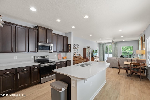 kitchen featuring a sink, stainless steel appliances, open floor plan, light wood-type flooring, and light countertops