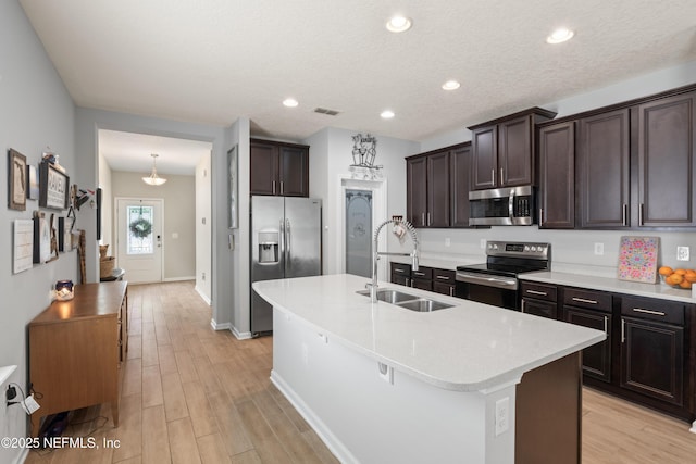 kitchen with a sink, dark brown cabinetry, stainless steel appliances, and light wood-style floors
