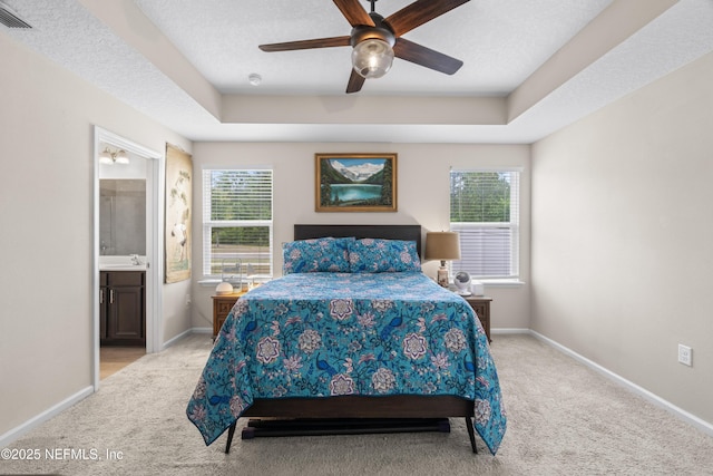 bedroom with light colored carpet, visible vents, a tray ceiling, connected bathroom, and baseboards