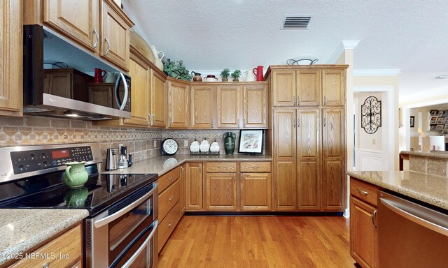 4637 Saddlehorn Trl, Middleburg, FL 32068 - kitchen featuring appliances with stainless steel finishes, decorative backsplash, light stone countertops, light wood finished floors, and a textured ceiling