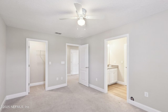 unfurnished bedroom featuring a spacious closet, light colored carpet, a closet, baseboards, and visible vents