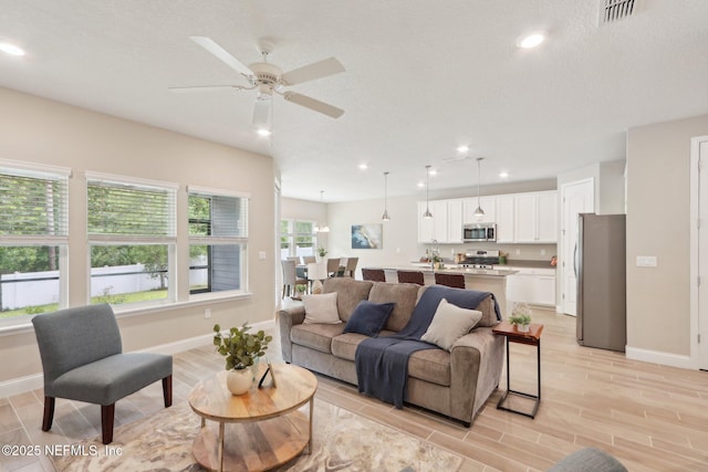 living room with visible vents, ceiling fan, light wood-style floors, and baseboards