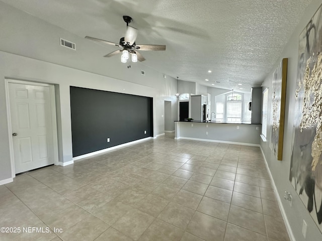 unfurnished living room with a ceiling fan, a textured ceiling, visible vents, a sink, and light tile patterned flooring