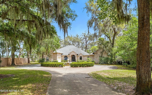 view of front of house with a front lawn, brick siding, curved driveway, and fence