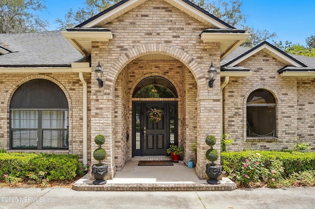 view of exterior entry featuring brick siding and a shingled roof