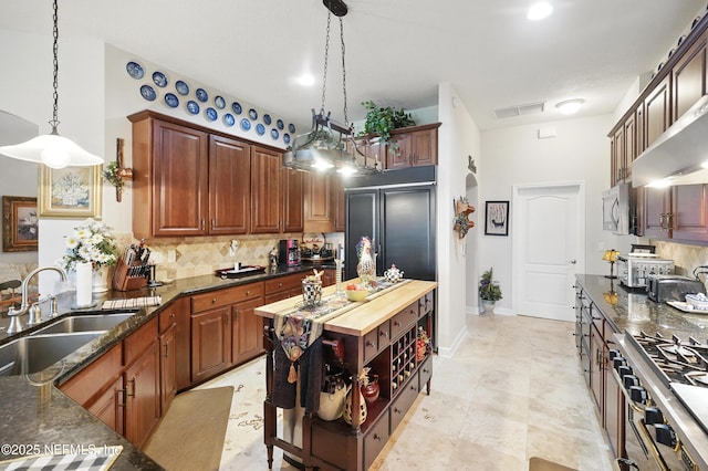 kitchen featuring tasteful backsplash, paneled built in refrigerator, a sink, visible vents, and pendant lighting