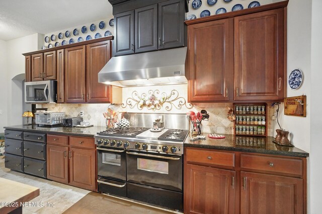 kitchen featuring dark stone countertops, double oven range, stainless steel microwave, under cabinet range hood, and backsplash