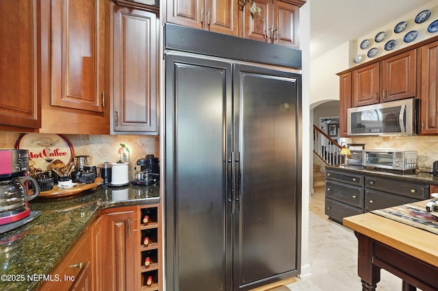 kitchen featuring stainless steel microwave, paneled built in fridge, backsplash, a toaster, and arched walkways