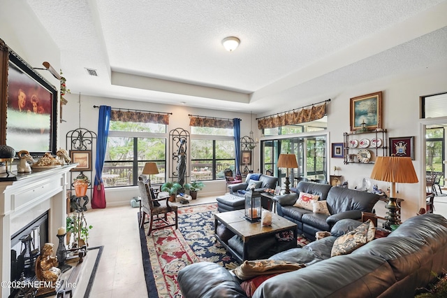 living area with a glass covered fireplace, a textured ceiling, visible vents, and a tray ceiling