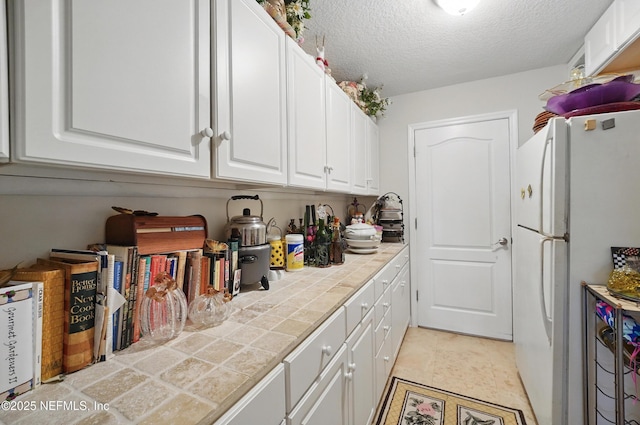 kitchen featuring white cabinetry, a textured ceiling, tile counters, and freestanding refrigerator