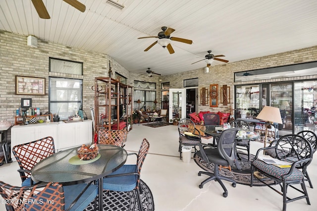 dining space with ceiling fan, finished concrete flooring, brick wall, and plenty of natural light