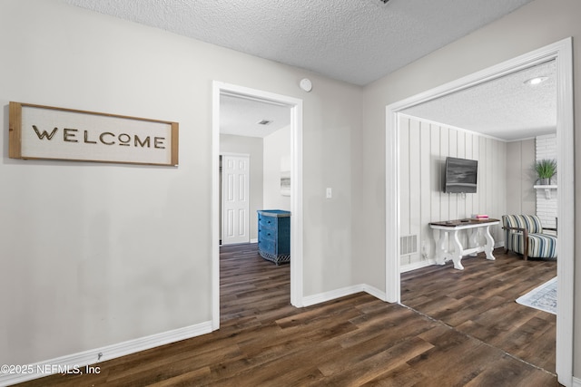 hall featuring baseboards, a textured ceiling, dark wood-style flooring, and visible vents