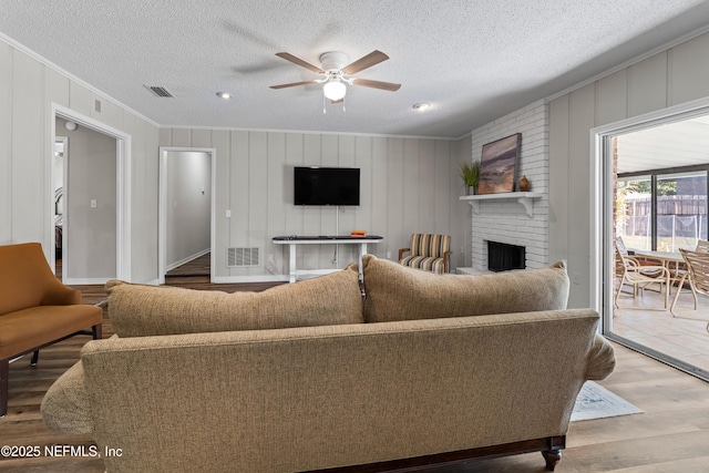 living room with crown molding, a ceiling fan, visible vents, and light wood finished floors