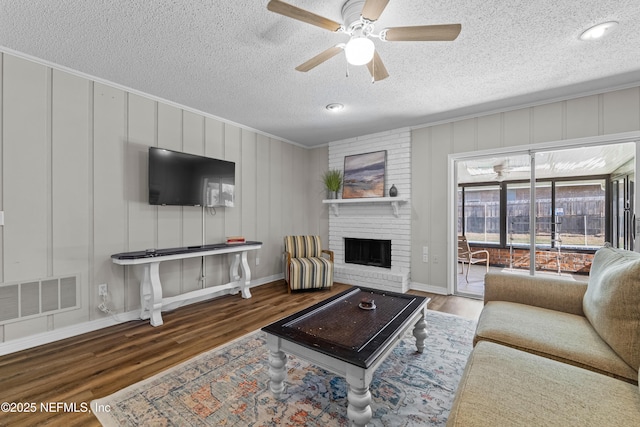 living area with a brick fireplace, a ceiling fan, baseboards, wood finished floors, and visible vents
