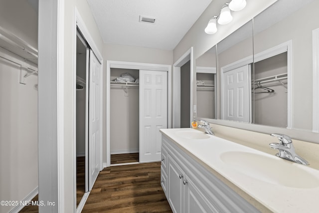 bathroom with double vanity, visible vents, a sink, and wood finished floors