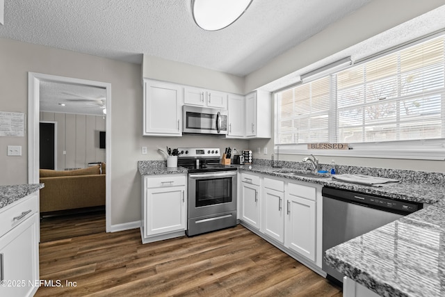 kitchen with light stone countertops, a textured ceiling, white cabinets, dark wood finished floors, and appliances with stainless steel finishes