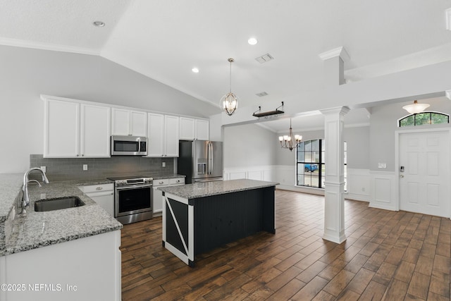 kitchen featuring wainscoting, appliances with stainless steel finishes, a kitchen island, a sink, and ornate columns