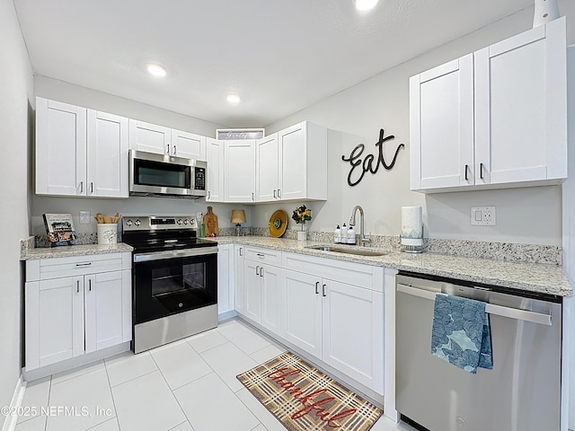 kitchen with light stone countertops, light tile patterned floors, stainless steel appliances, a sink, and white cabinetry