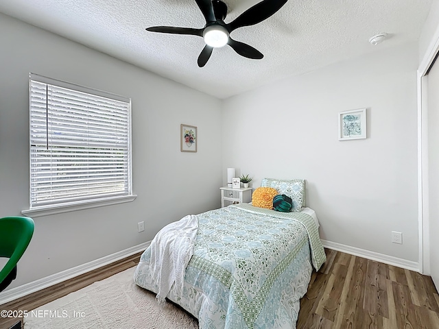bedroom featuring baseboards, wood finished floors, ceiling fan, and a textured ceiling