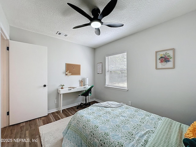 bedroom with a ceiling fan, visible vents, baseboards, a textured ceiling, and wood finished floors