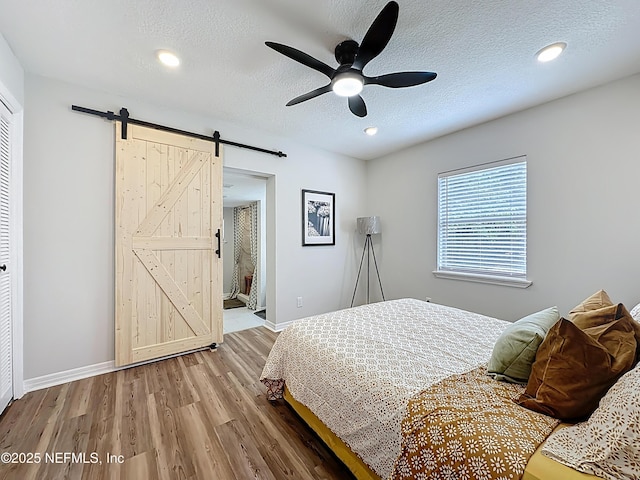 bedroom with recessed lighting, a barn door, baseboards, a textured ceiling, and wood finished floors