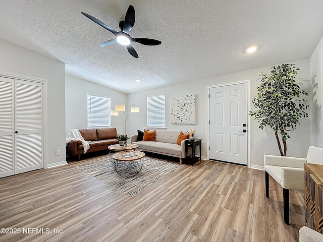 living room with baseboards, a ceiling fan, a textured ceiling, and light wood-style flooring