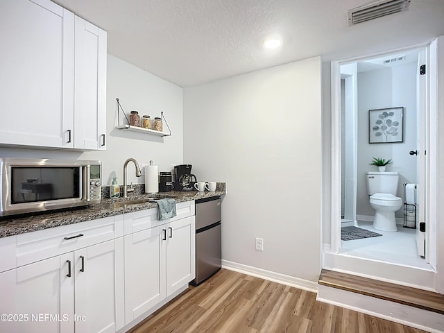 kitchen with dark stone countertops, refrigerator, stainless steel microwave, light wood finished floors, and visible vents