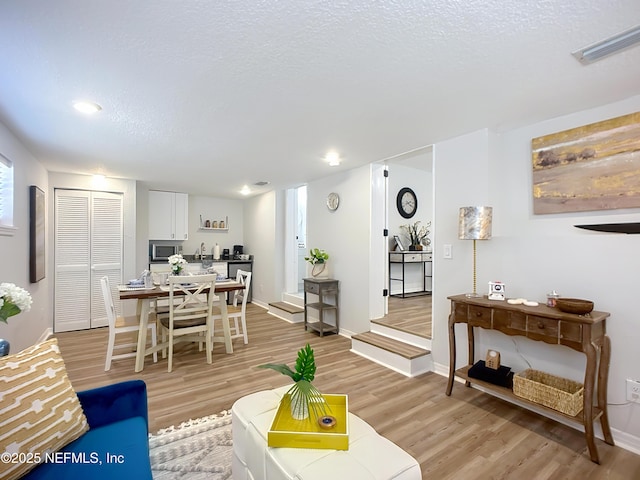 living area with recessed lighting, light wood-style floors, baseboards, visible vents, and a textured ceiling